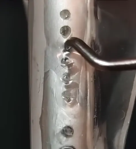 A metal pick tool being used to dig dust out of a phone speaker grille