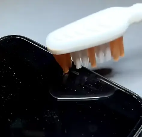 A soft brush removing dust from a phone speaker grille