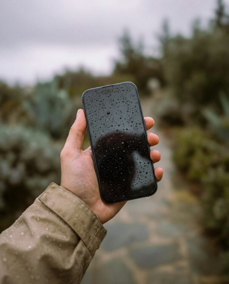 Hand holding a wet smartphone outdoors after rain, illustrating water-related speaker muffling